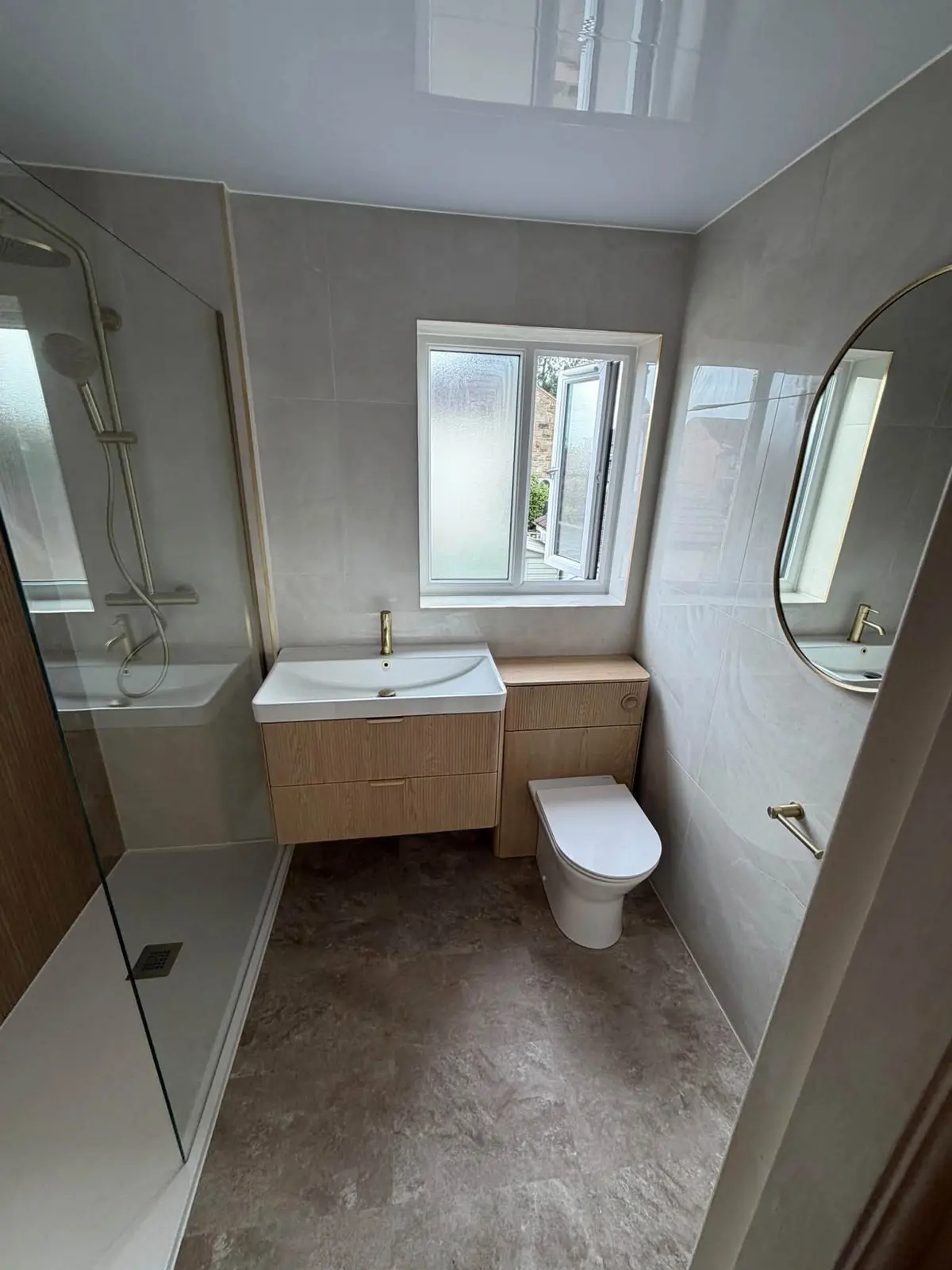 A bathroom Smartfix fitted: a walk-in shower, a wooden vanity unit with a brass tap, and an oval mirror